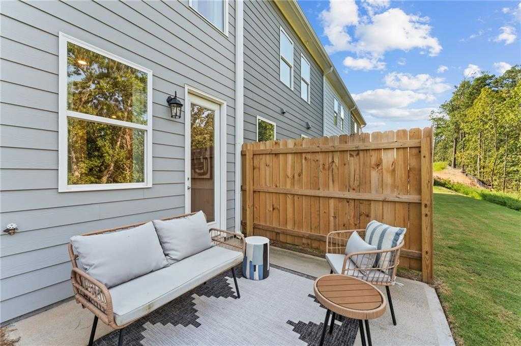 Cozy patio with wicker loveseat, armchair, and teak tables beside gray two-story home, wooden privacy fence, lush green yard in Stegall Village, Emerson, Georgia
