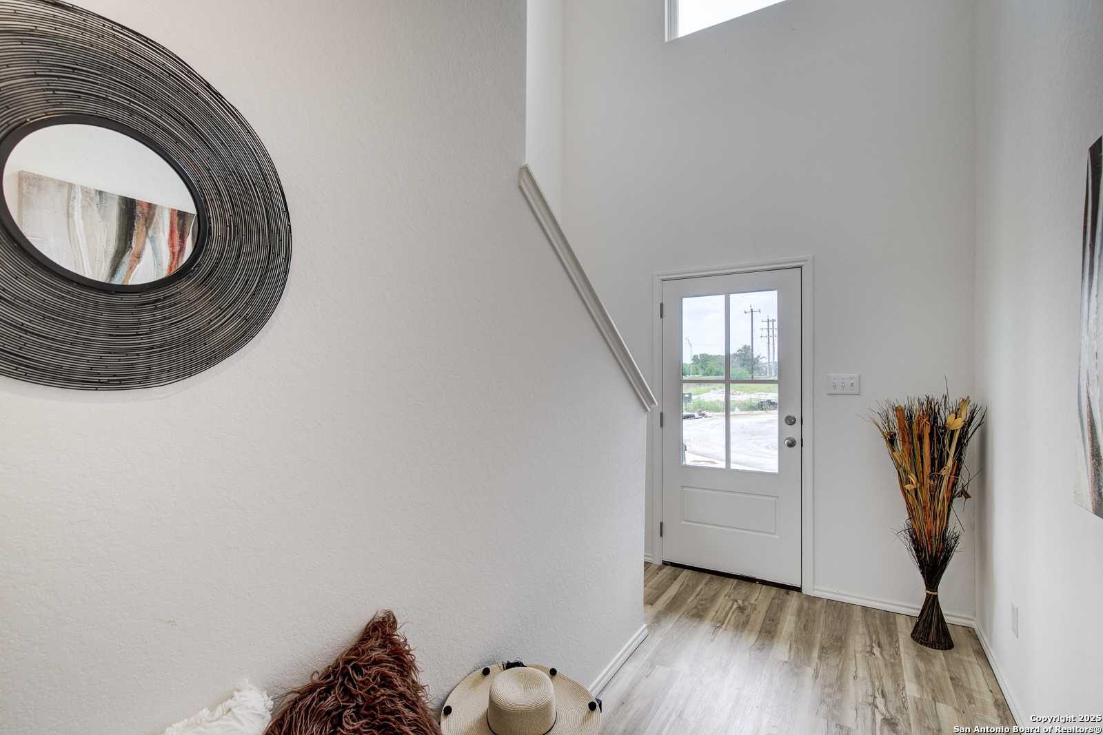 Bright entryway featuring circular mirror, open staircase, and glass-paneled door in Davidson Homes The Trinity A, San Antonio