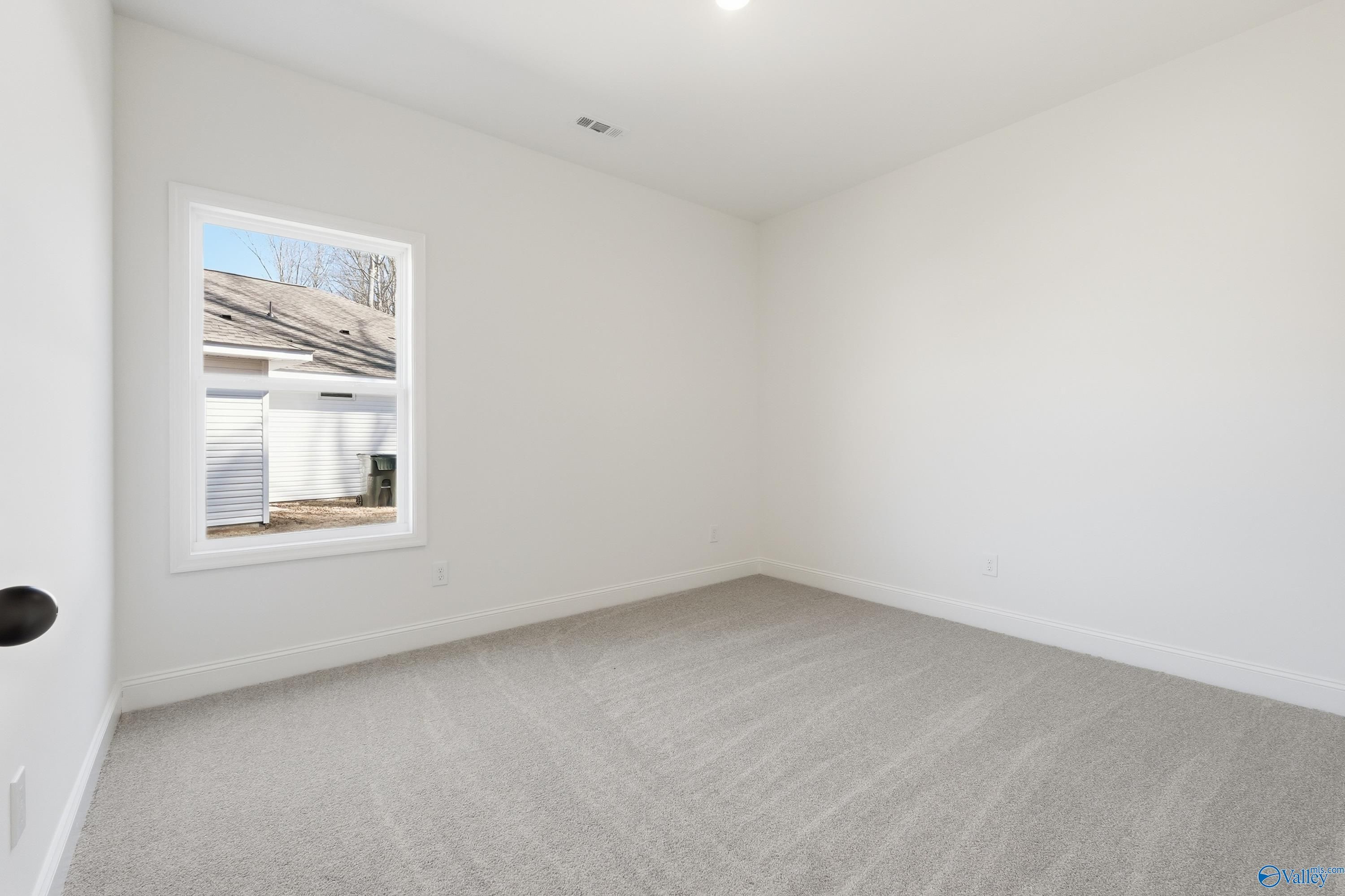 Empty bedroom featuring gray carpet, white walls, and large window overlooking exterior in The Rockford D, Hazel Green, AL