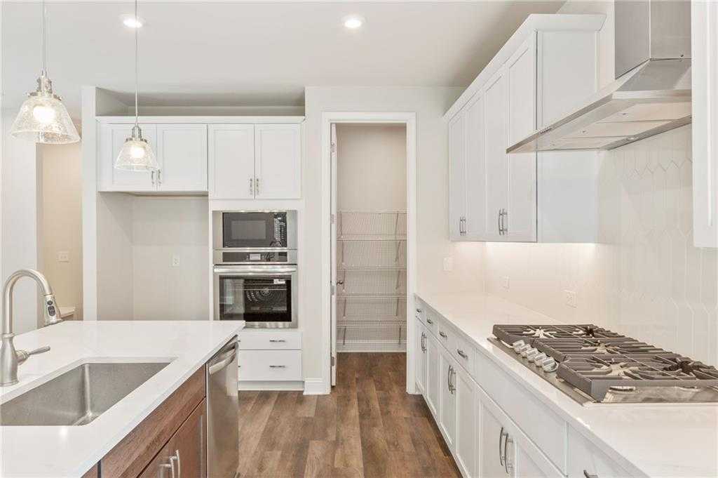 Modern white shaker kitchen with island sink, stainless double oven, gas range, and pantry in The Danbury E, Buford, GA