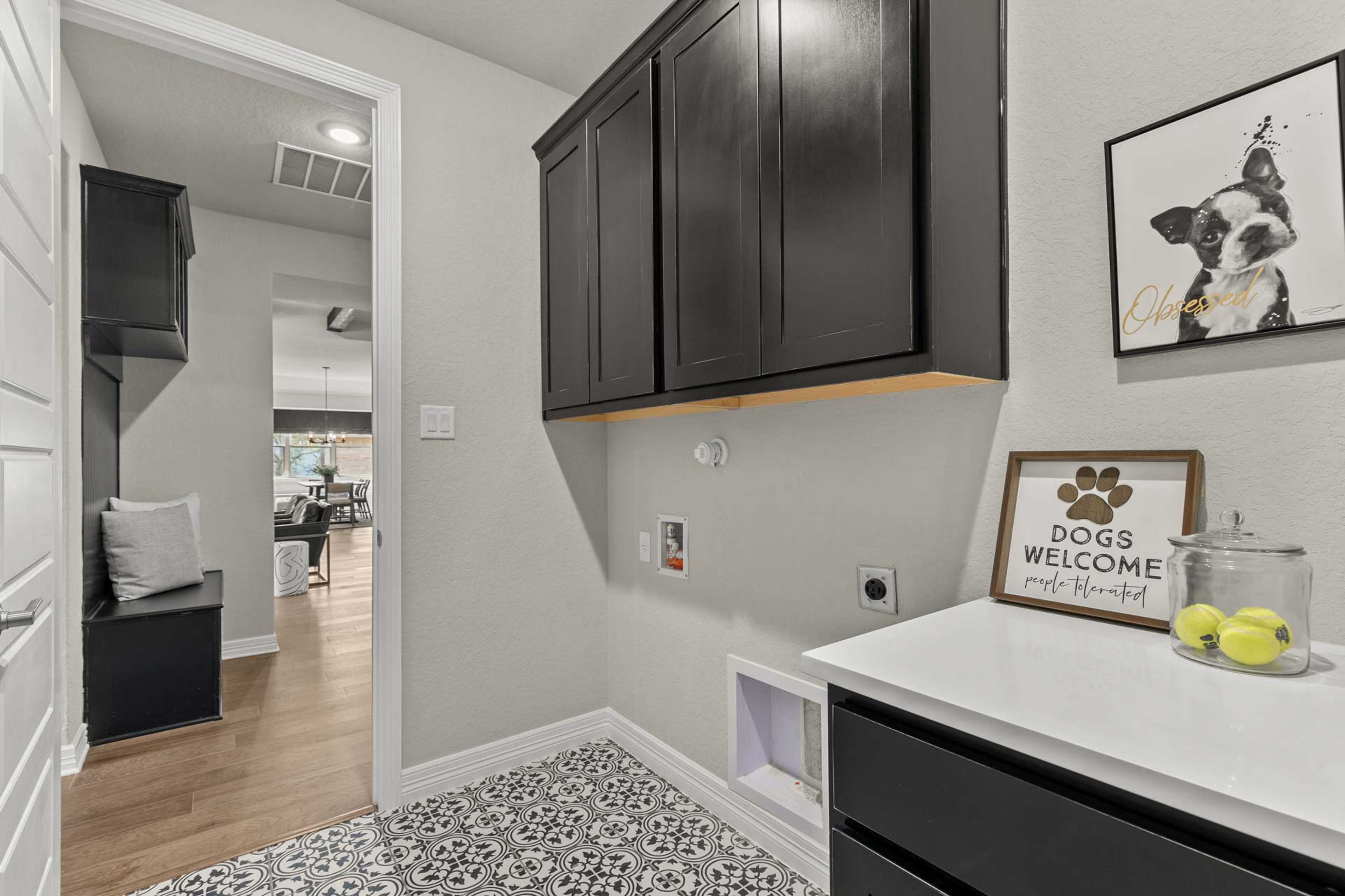 Spacious laundry mudroom in Potranco Oaks, Castroville TX with dark cabinets, pet door, dog welcome sign, and tiled floor by Davidson Homes