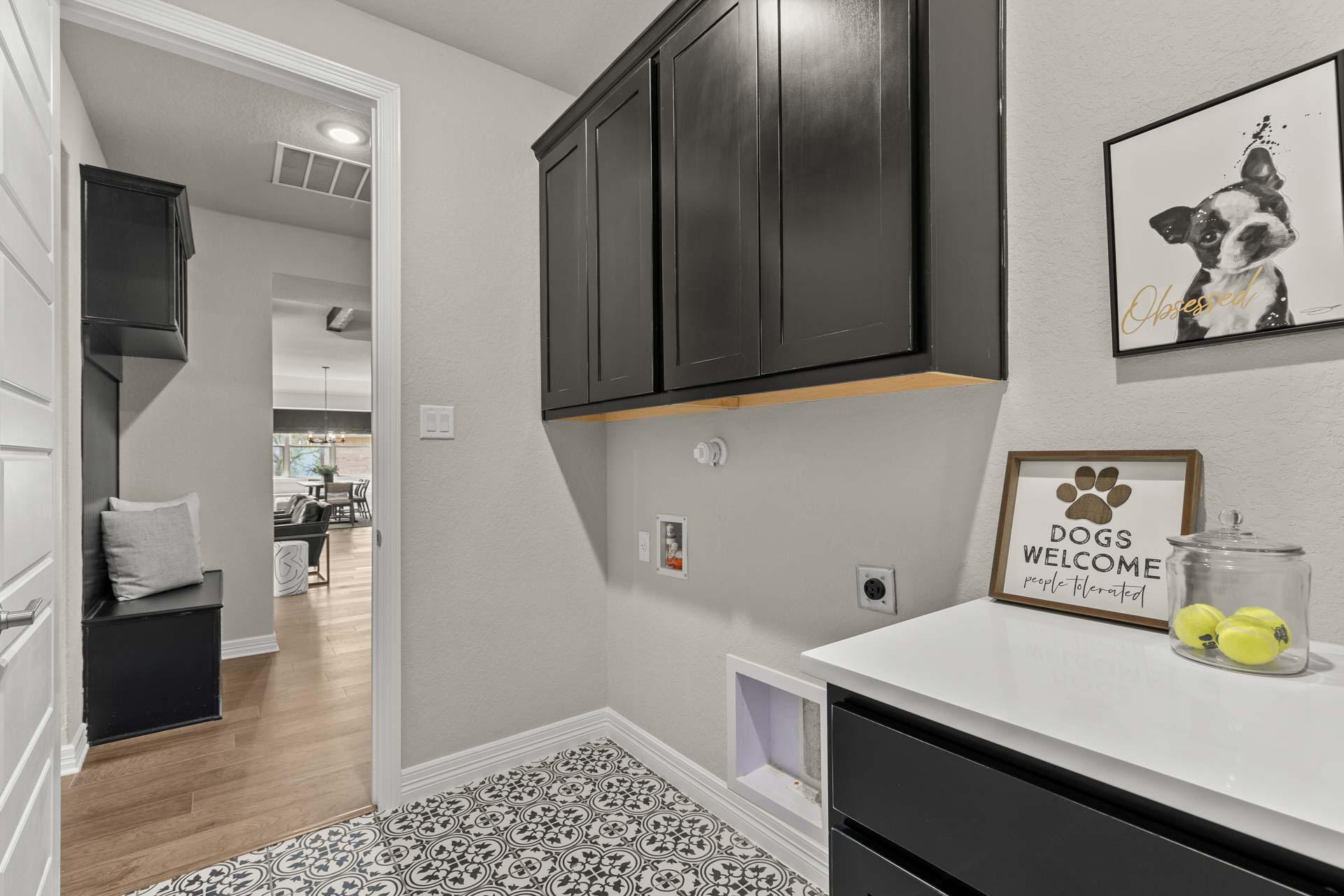 Spacious laundry mudroom in Potranco Oaks, Castroville TX with dark cabinets, pet door, dog welcome sign, and tiled floor by Davidson Homes