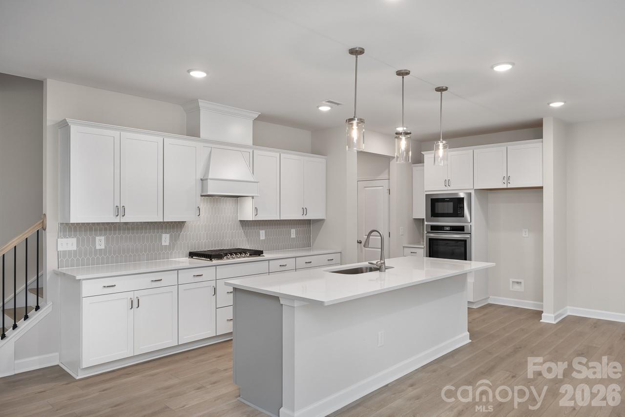 Modern white kitchen featuring quartz island, stainless double ovens, gas range, and herringbone backsplash in Davidson Homes The Beech B, Belmont NC