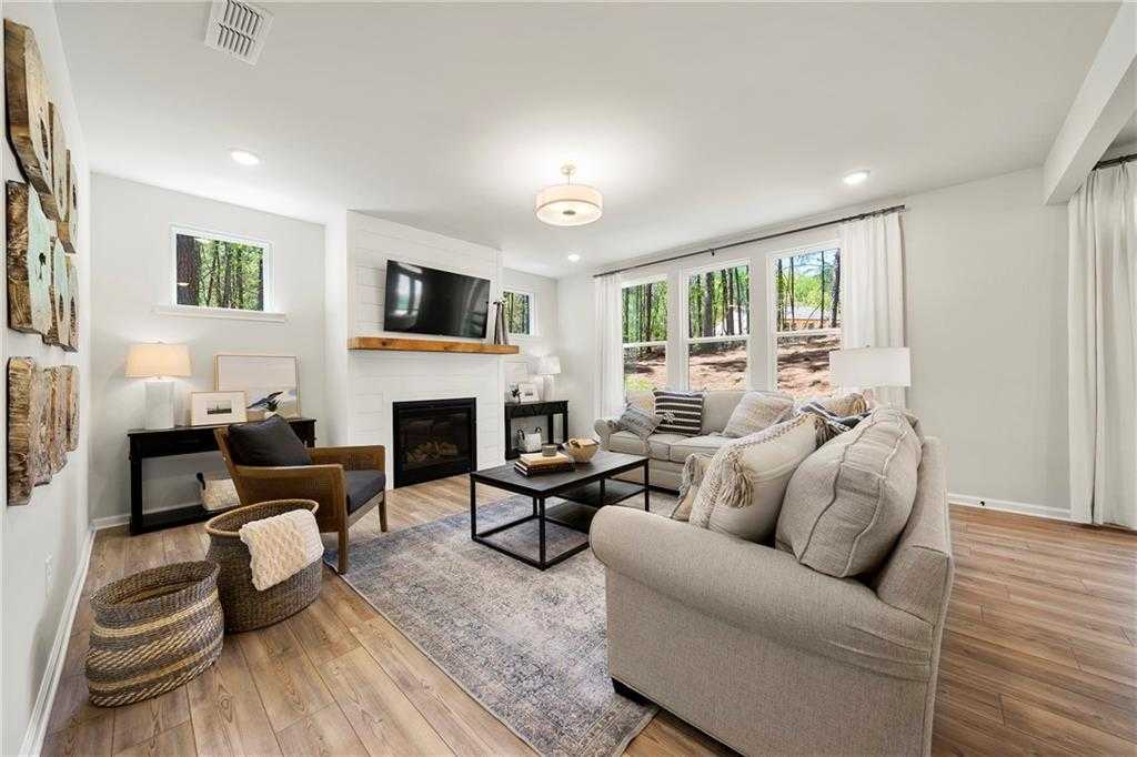 Cozy living room with gas fireplace, mounted TV, plush sectional sofa, and wooded window views in Davidson Homes The Hickory B, Riverwood, Dallas, Georgia