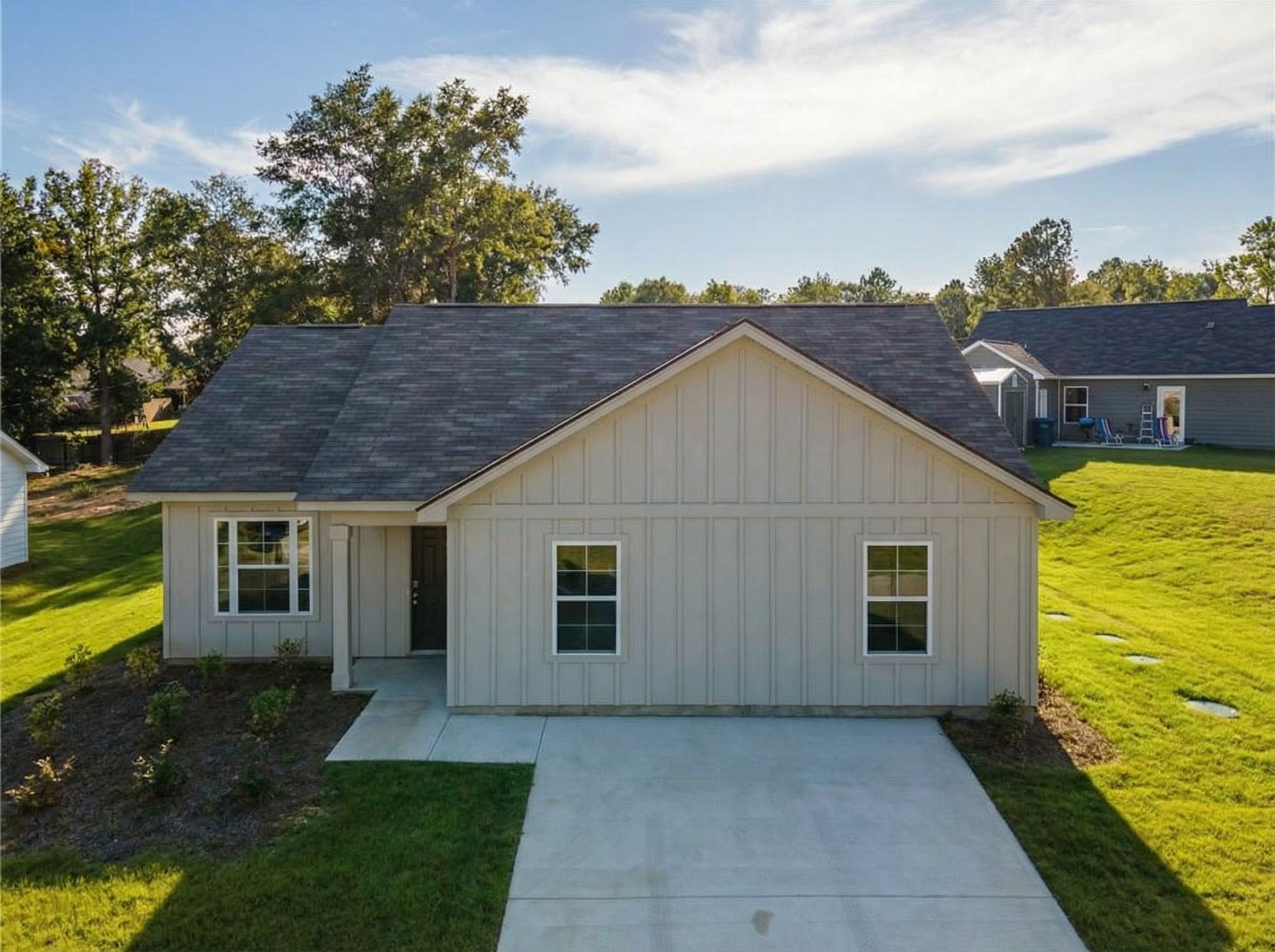 Aerial view of modern 3-bedroom single-story home with gray siding, shingled roof, driveway, and landscaped yard in Heatherbrook, Phenix City, Alabama