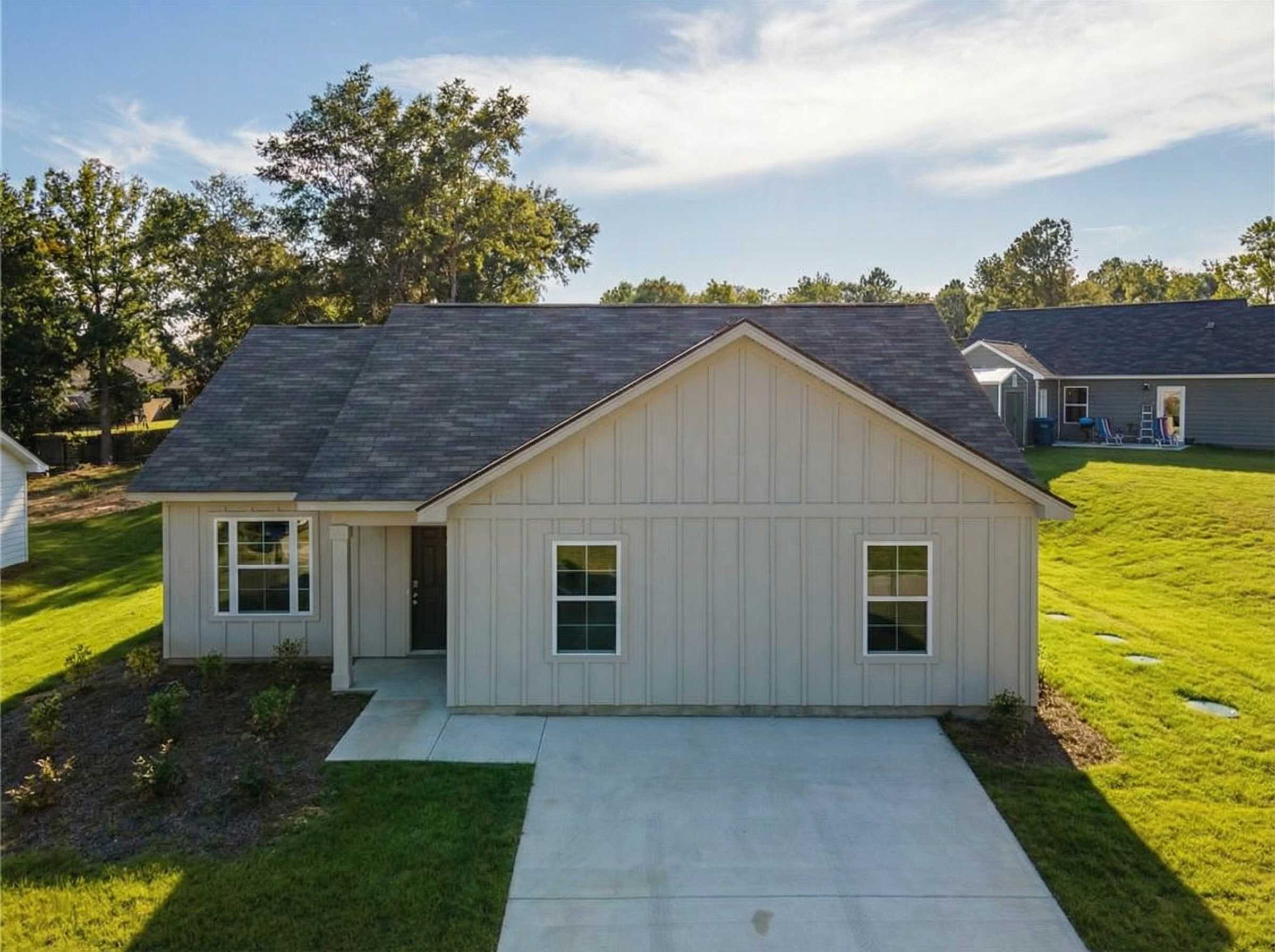 Aerial view of modern 3-bedroom single-story home with gray siding, shingled roof, driveway, and landscaped yard in Heatherbrook, Phenix City, Alabama
