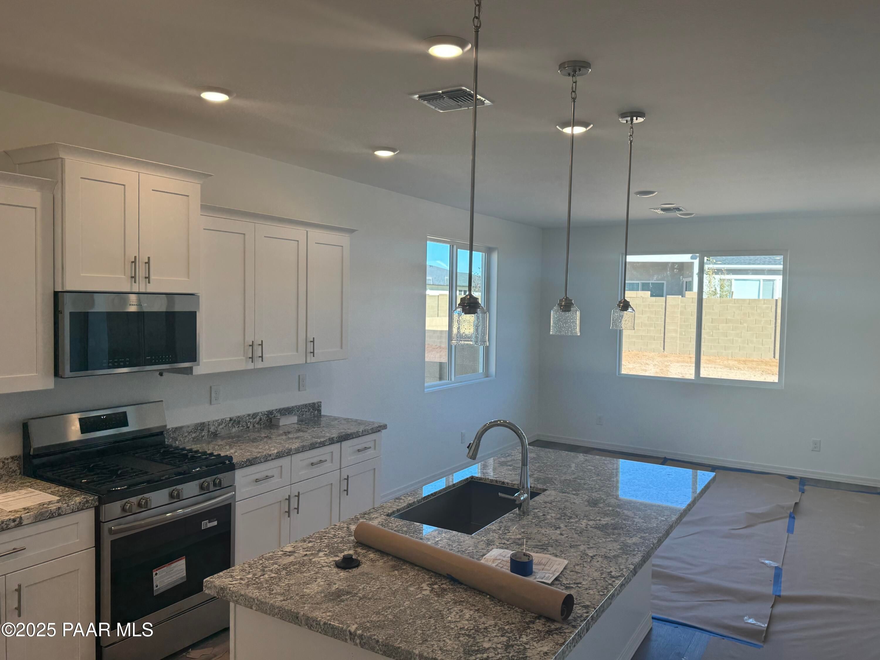 Modern kitchen with granite island, stainless appliances, white cabinets, pendant lights in Davidson Homes The Summit A, Prescott, AZ