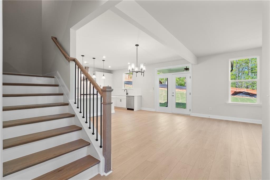 Grand wooden staircase with iron balusters overlooking open kitchen, white cabinets, and French doors to yard in Davidson Homes The Hickory E, Buford GA