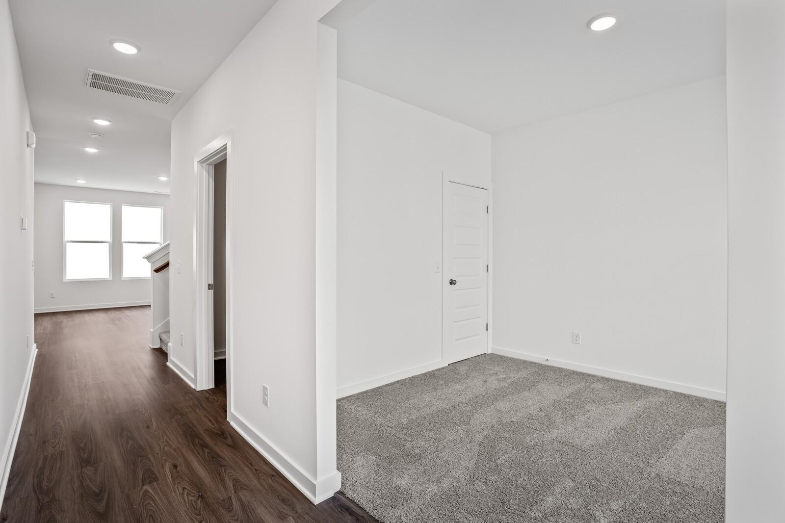 Bright upstairs hallway with white walls, hardwood floors, and carpeted bedroom in Davidson Homes The Logan C, White House TN