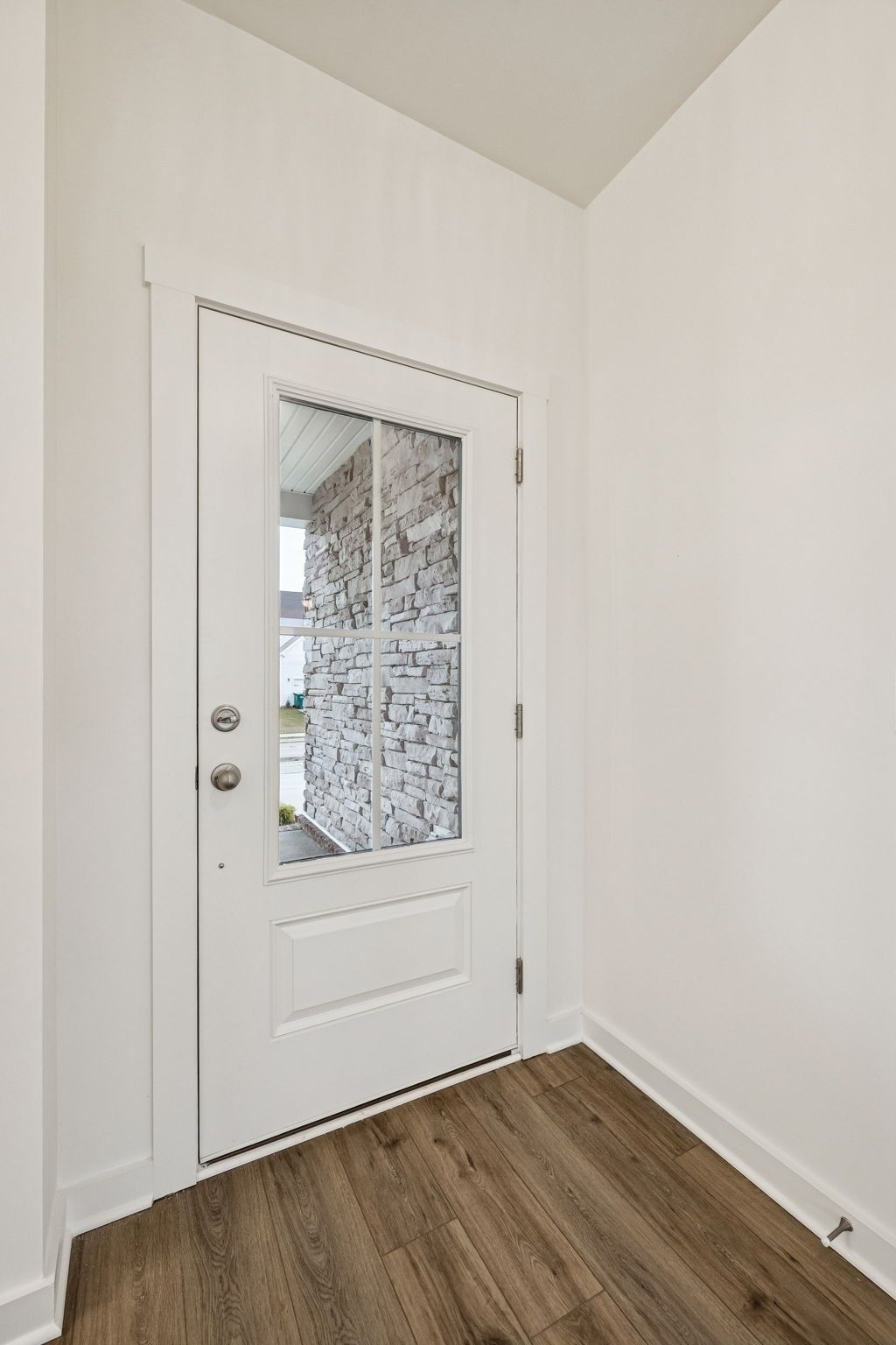 White entry door with glass panels showing brick exterior and hardwood flooring in Davidson Homes The Willow