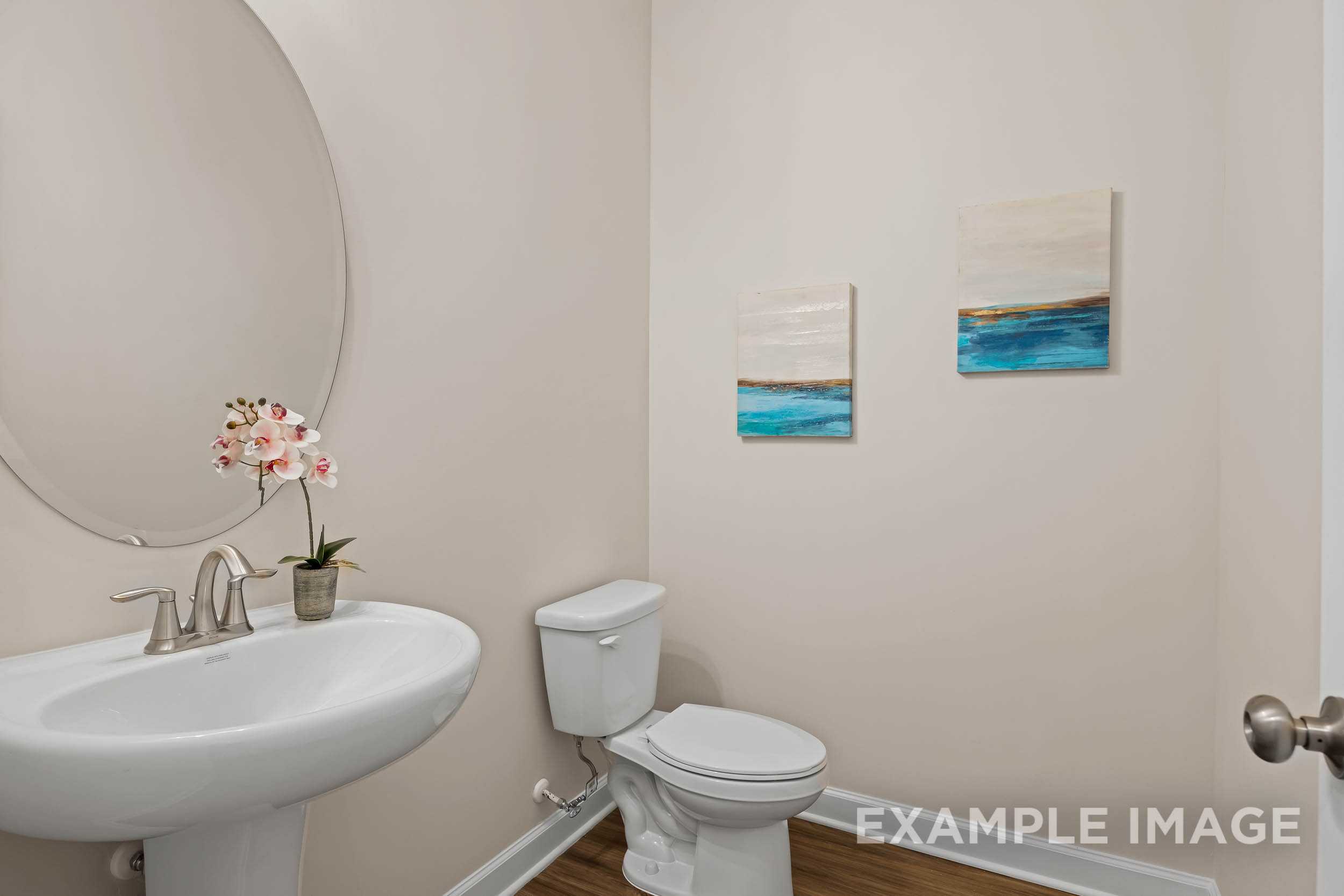 Spacious powder room in The Preston A home design with pedestal sink, round mirror, and abstract wall art