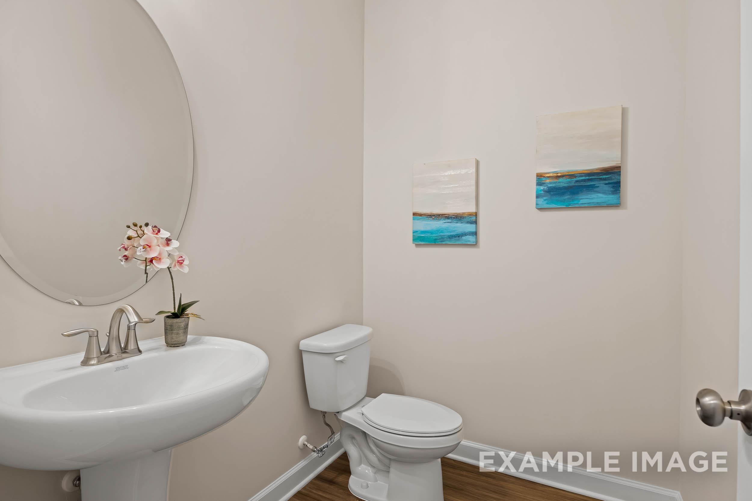 Spacious powder room in The Preston A home design with pedestal sink, round mirror, and abstract wall art