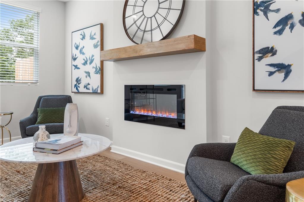 Cozy living room featuring electric fireplace with flames, wooden mantel, round mirror, blue bird wall art, gray armchairs, and marble coffee table in Davidson Homes The Durant A, Emerson, Georgia