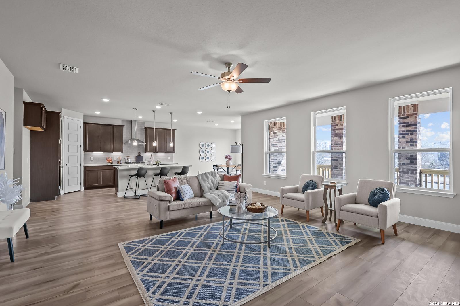 Spacious open-concept living room with gray sofa, ceiling fan, large windows, and kitchen island in Davidson Homes The Rockford G, Ladera, San Antonio