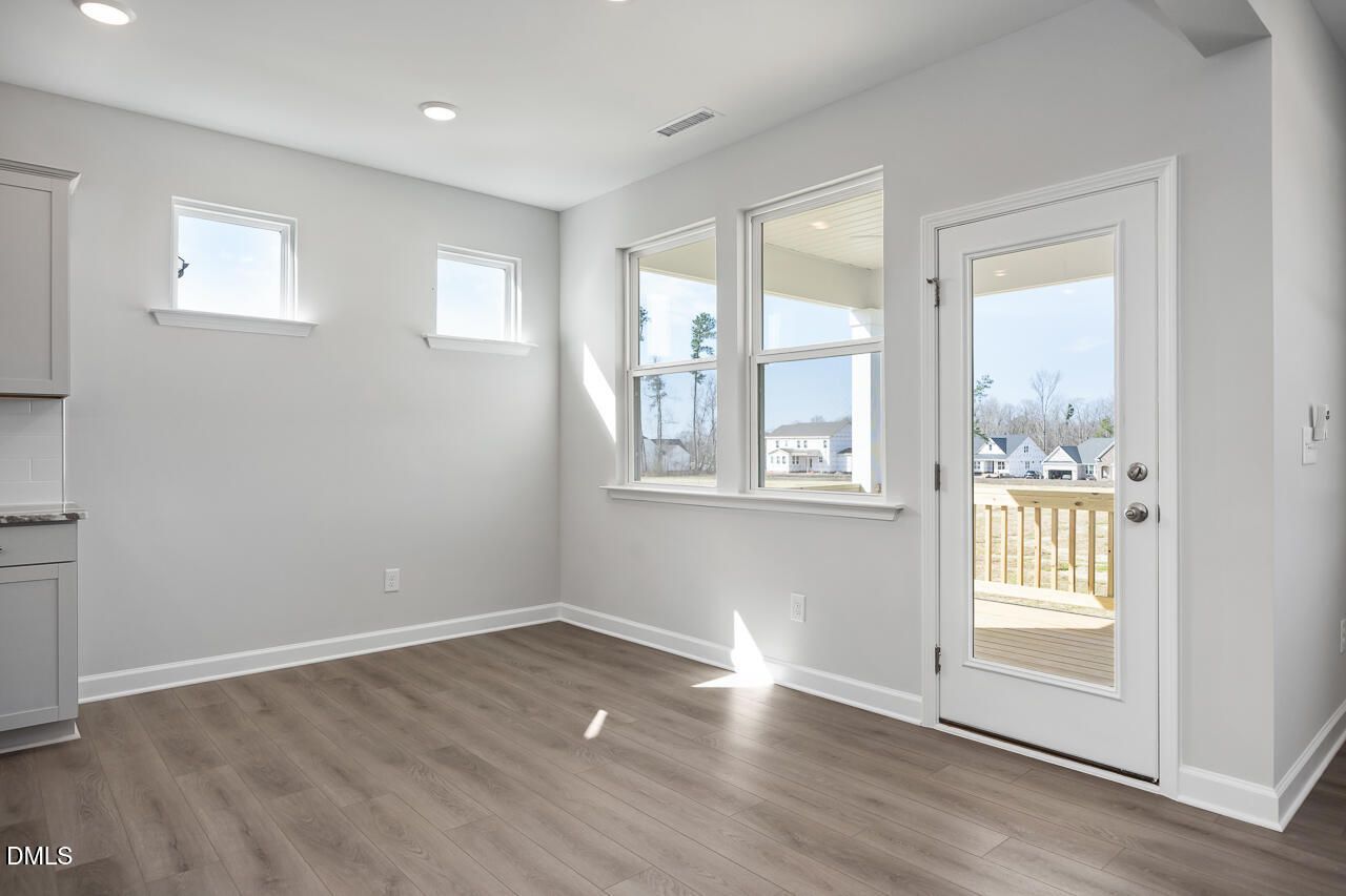 Bright sunlit room with gray walls, hardwood floors, large windows, and deck door in 5-bedroom Davidson Homes The Willow G, Angier, NC