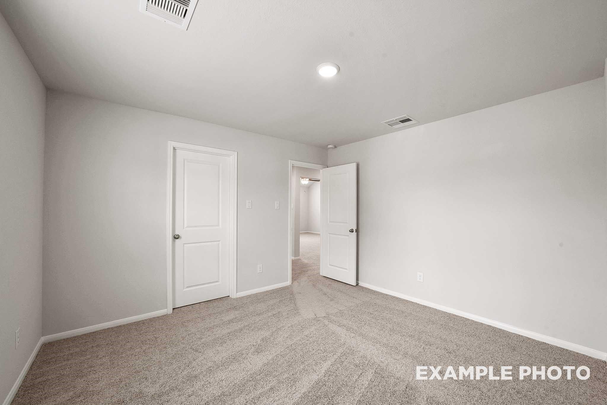 Spacious secondary bedroom with beige carpet, neutral walls, and adjacent doorways in Davidson Homes The Tierra B, Beasley, Texas