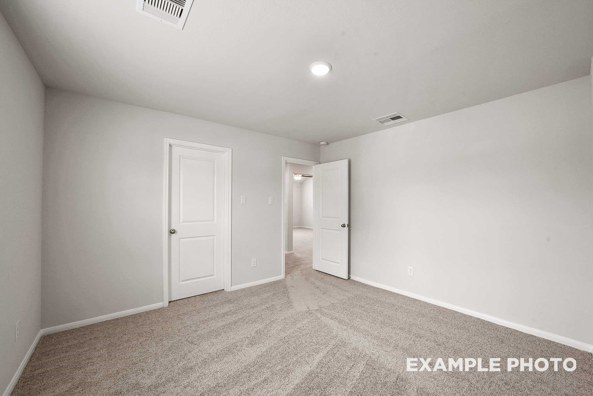 Spacious secondary bedroom with beige carpet, neutral walls, and adjacent doorways in Davidson Homes The Tierra B, Beasley, Texas