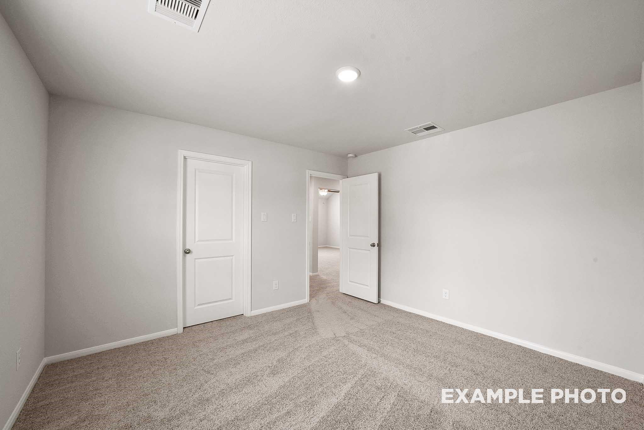 Empty secondary bedroom featuring light gray walls, white doors, and beige carpet in Davidson Homes The Tierra B, Beasley, Texas