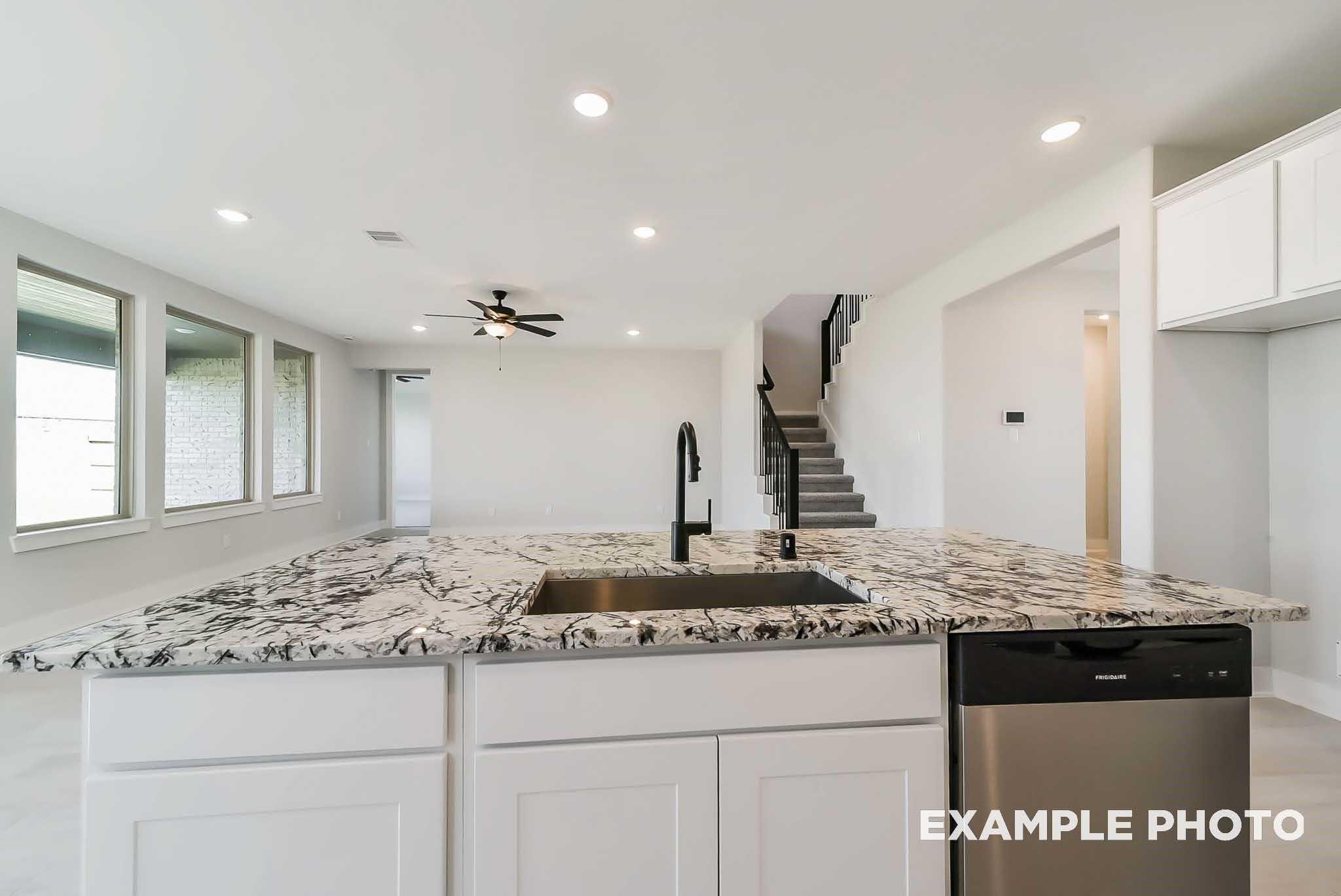 Modern kitchen island with veined marble counters, stainless sink, dishwasher, and white cabinets in Davidson Homes The Philip C, Rosharon, Texas