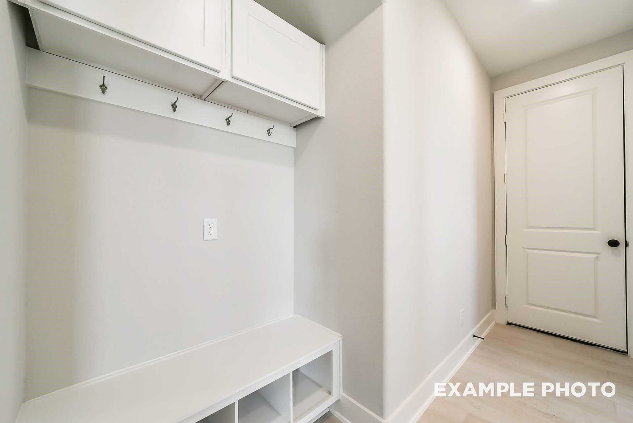 Modern white mudroom with built-in bench, coat hooks, and upper cabinets in Davidson Homes The Philip C, Rosharon, Texas