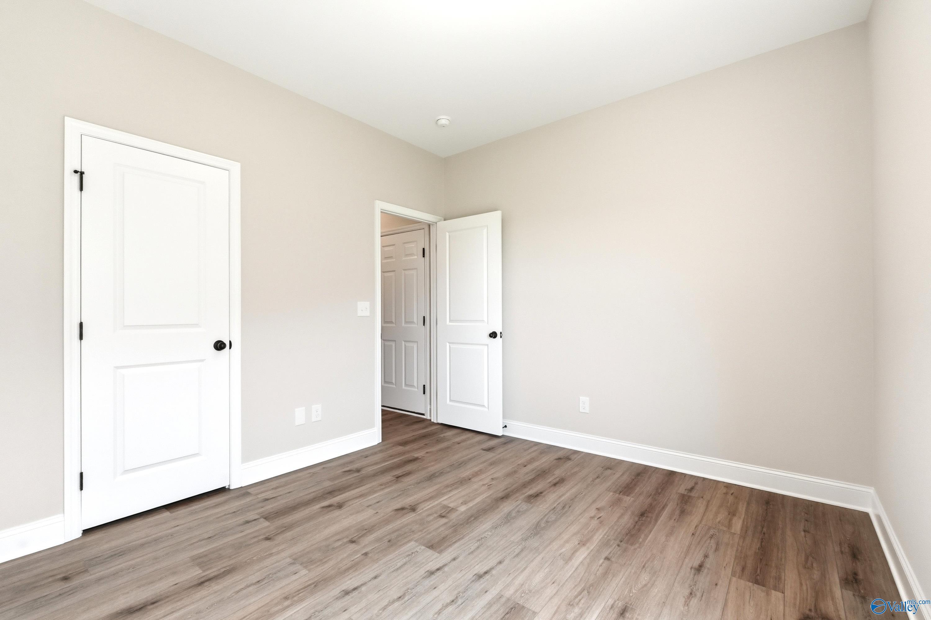 Neutral-toned bedroom with wood-look flooring and white doors in The Daphne floor plan, Clearview, Hazel Green, Alabama.