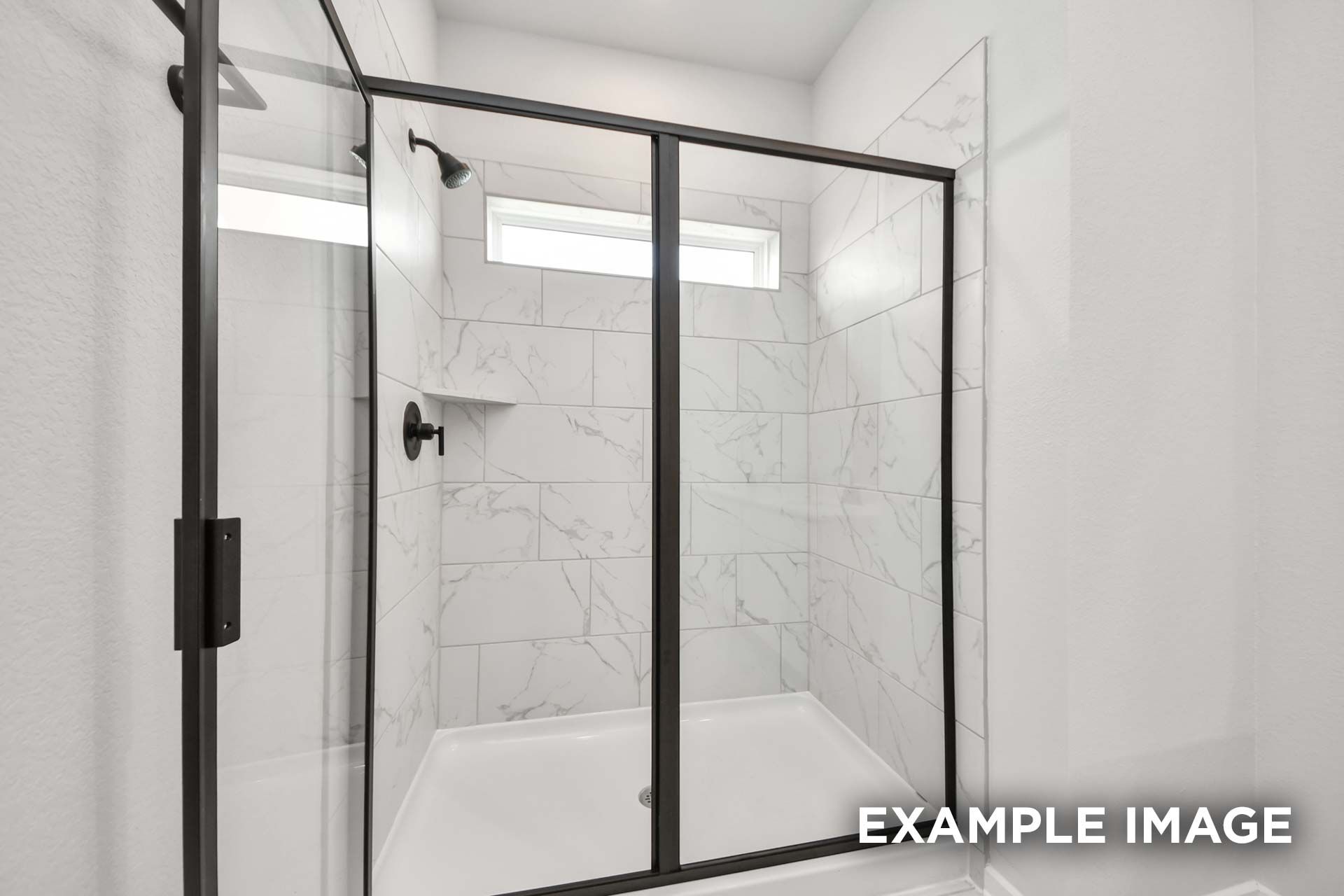 Modern walk-in shower with black frame, marble-look tile, and transom window in The Sorrento master suite.
