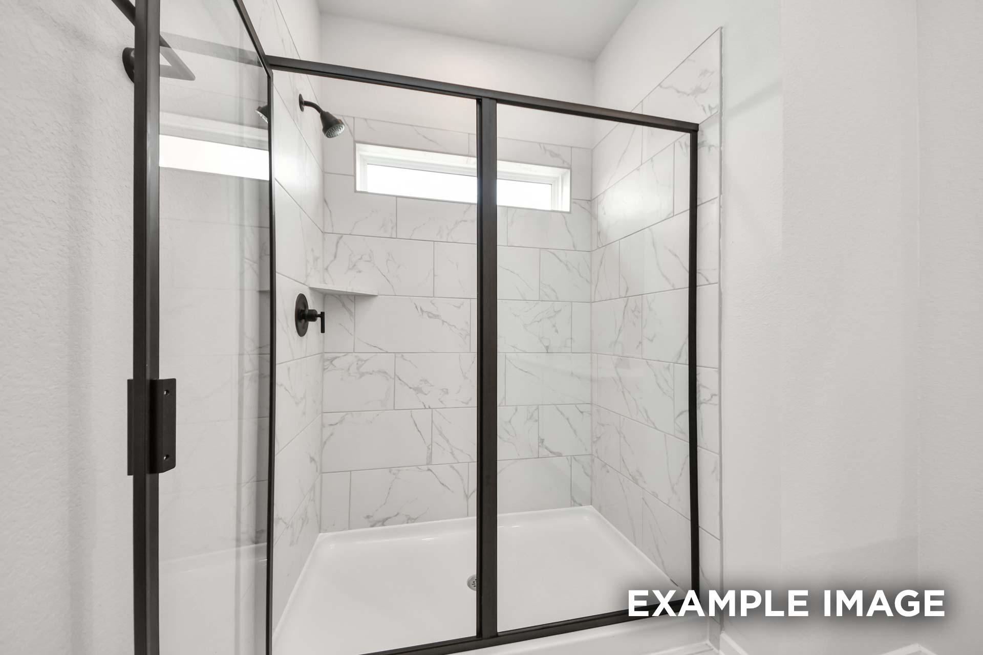 Modern walk-in shower with black frame, marble-look tile, and transom window in The Sorrento master suite.