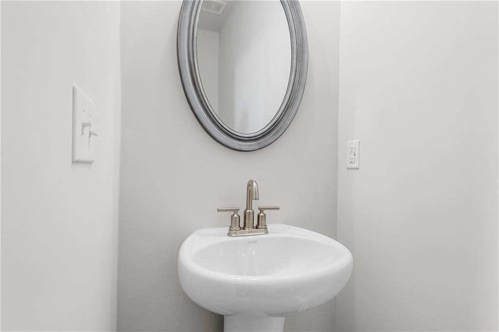 Modern powder room with pedestal sink and oval mirror in The Glenwood A floor plan at Wehunt Meadows, Hoschton, GA.