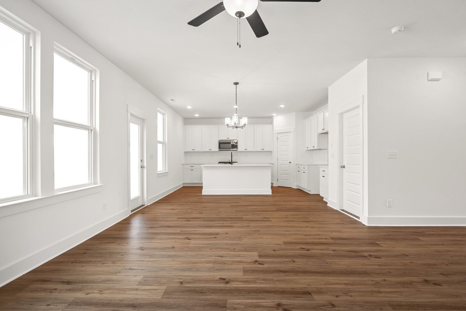 Bright open-concept kitchen and living space with white cabinets, center island, hardwood floors, and large windows in Davidson Homes The Logan C, Gallatin, TN