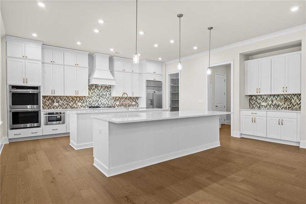 Modern white kitchen with large island, stainless appliances, metallic tile backsplash, and hardwood floors in Davidson Homes The Arlington A, East Cobb, GA