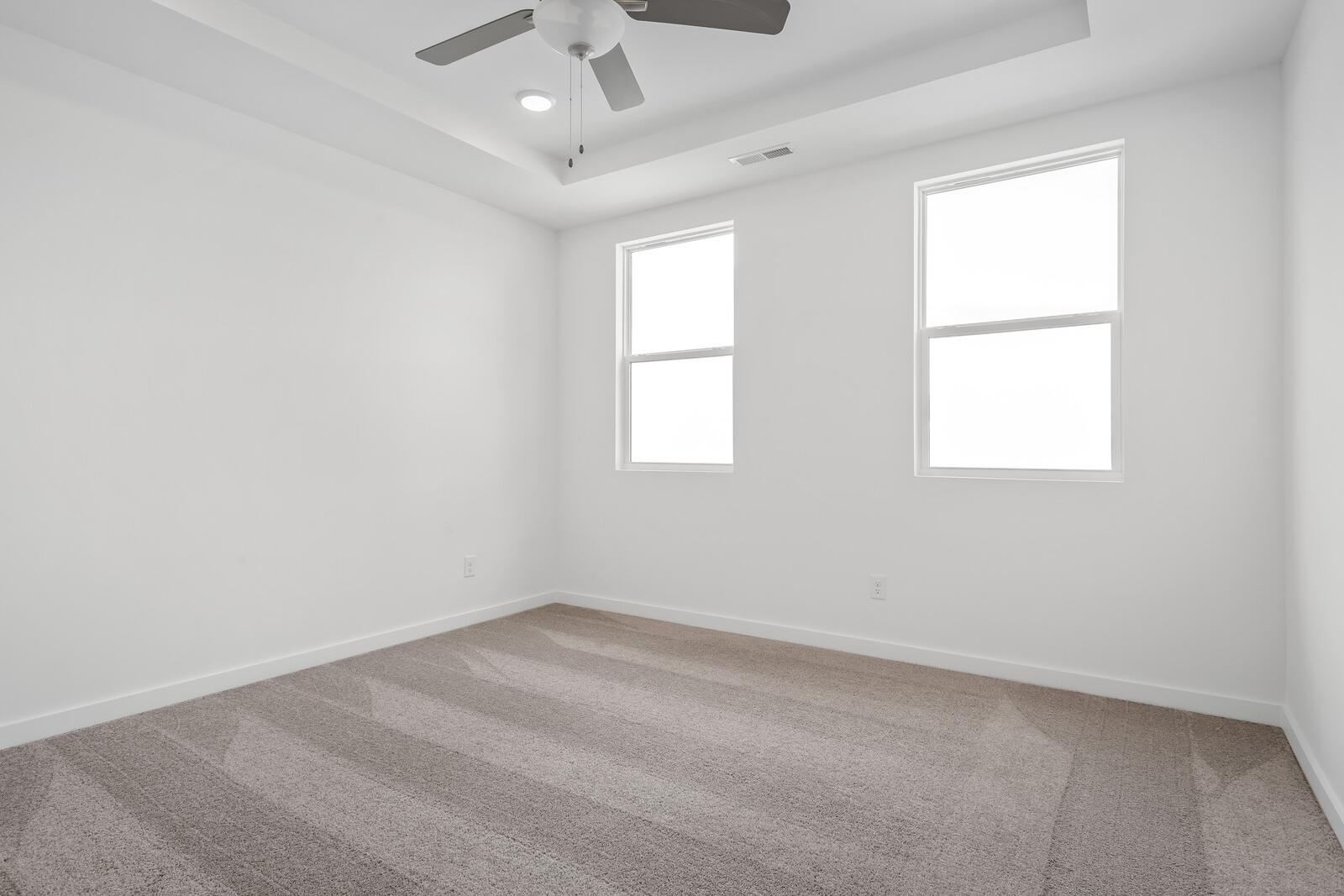 Spacious empty bedroom in The Asheville home with white walls, dual windows, ceiling fan, and neutral carpet flooring