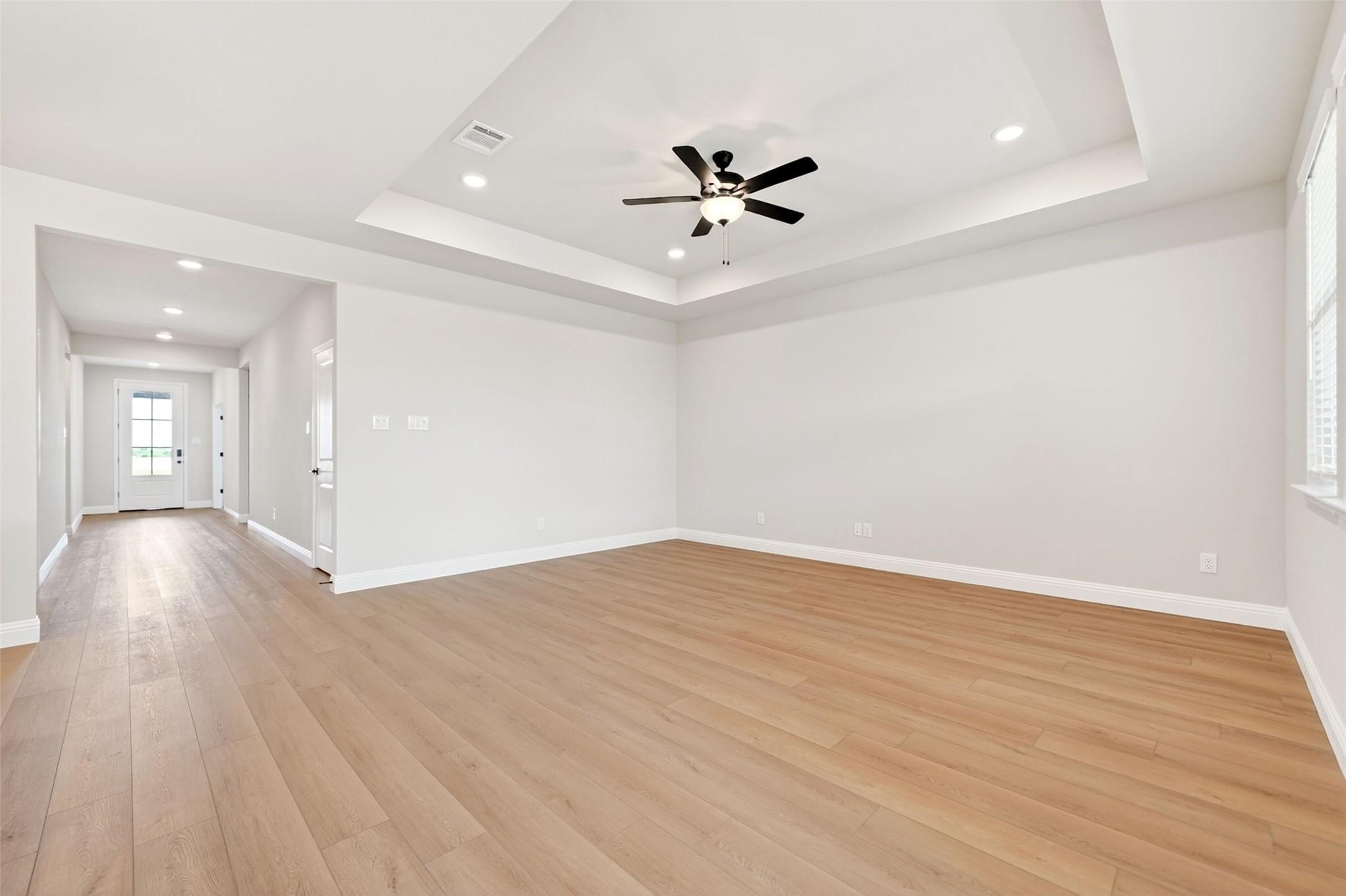 Spacious living area with tray ceiling and light wood floors in The Holly C floor plan by Davidson Homes in Anna, Texas.