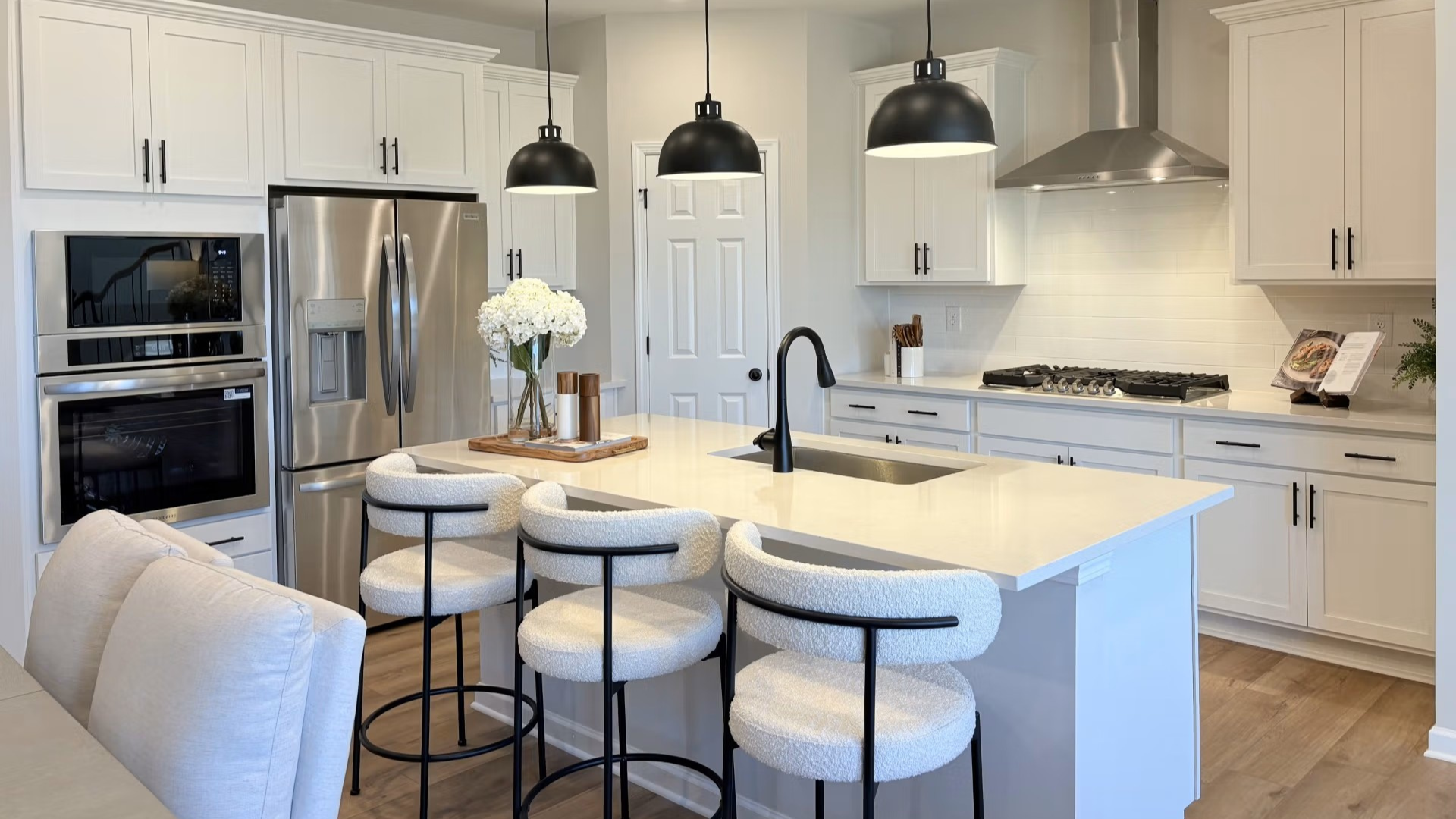 Spacious Hemingway model kitchen with white shaker cabinets, quartz island, stainless appliances, upholstered bar stools, fresh flowers