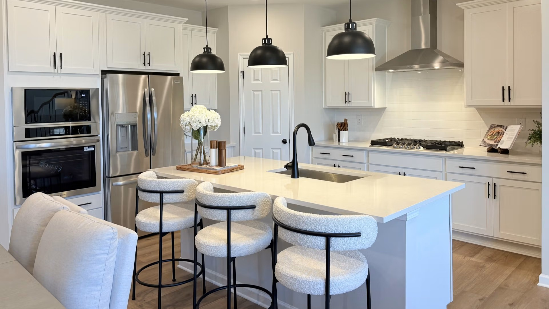 Spacious Hemingway model kitchen with white shaker cabinets, quartz island, stainless appliances, upholstered bar stools, fresh flowers
