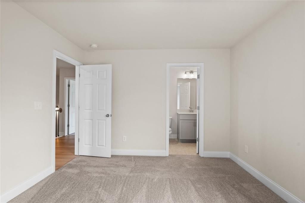 Spacious secondary bedroom with beige walls, gray carpet, and attached bath in Davidson Homes The Hickory B at Wehunt Meadows, Hoschton