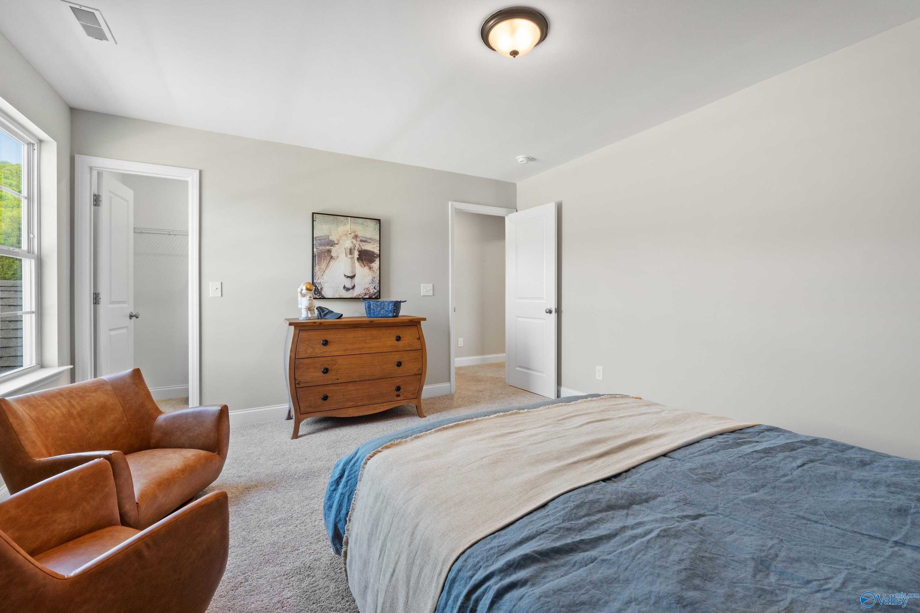 Cozy bedroom with wooden dresser, leather armchairs, framed cow artwork, and plush blue bed in Evermore Homes The Haven, Owens Cross Roads, AL