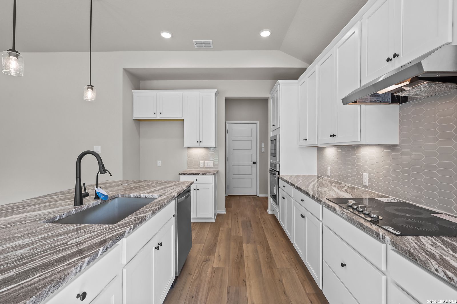 Modern kitchen with white shaker cabinets, granite countertops, island sink, and hardwood floors in Davidson Homes' The Sequoia C, San Antonio