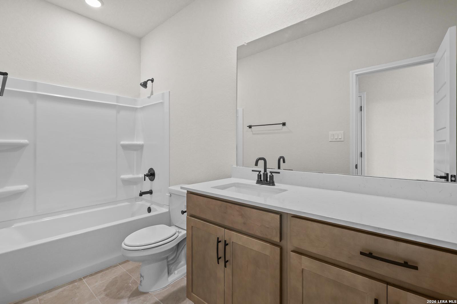 Modern bathroom with tub-shower combo, wood vanity, and white quartz countertop in Davidson Homes Glenwood E, San Antonio, Texas