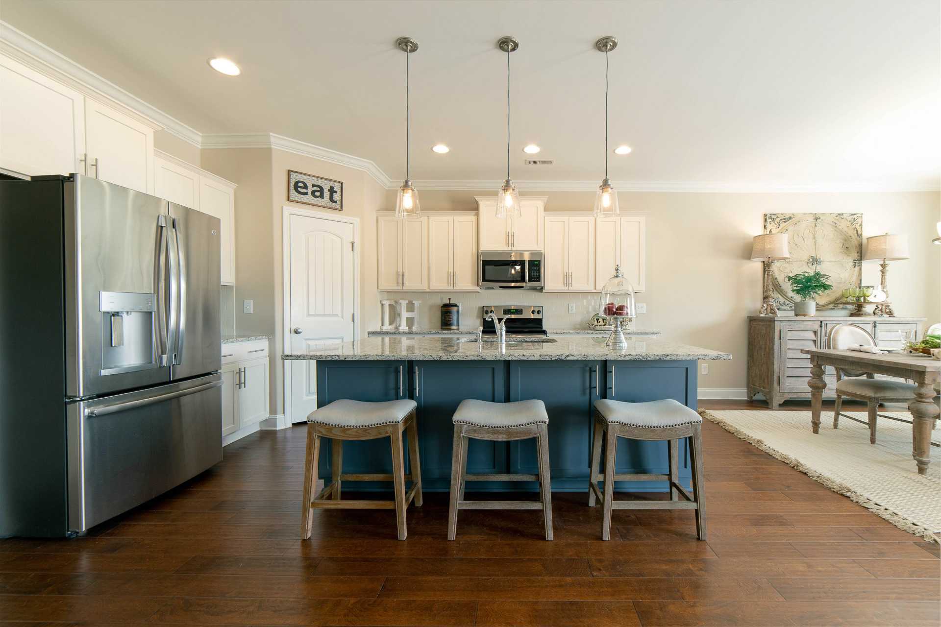 Spacious kitchen at The Dairy at Oak Grove in South Huntsville AL with white cabinets, quartz island, blue stools and hardwood floors