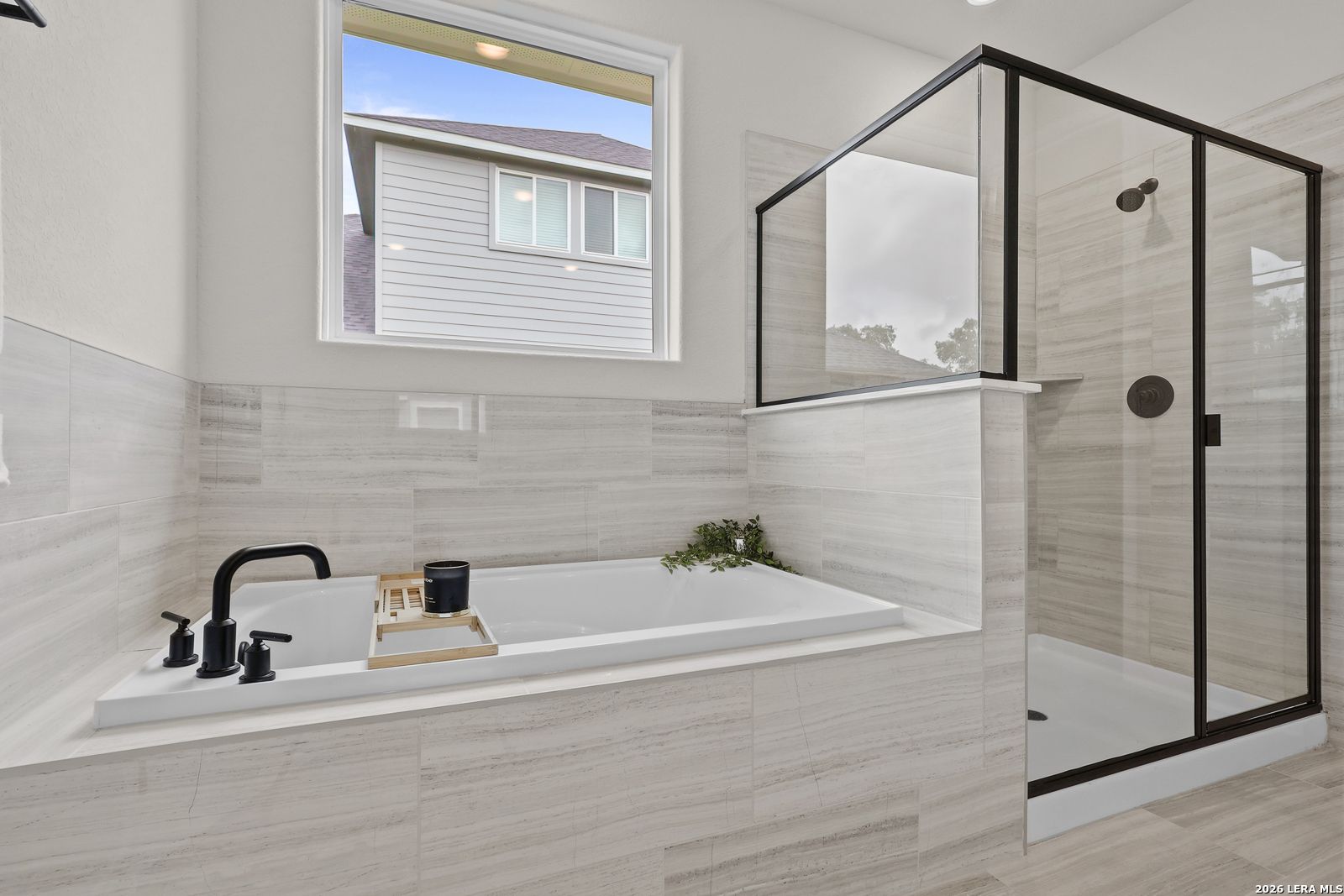 Elegant master bathroom with soaking tub, black fixtures, glass shower, marble tiles in The Lanier G, Castroville TX