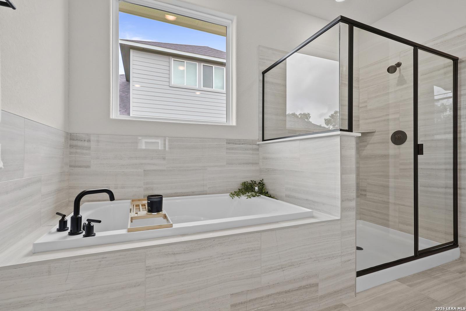 Elegant master bathroom with soaking tub, black fixtures, glass shower, marble tiles in The Lanier G, Castroville TX