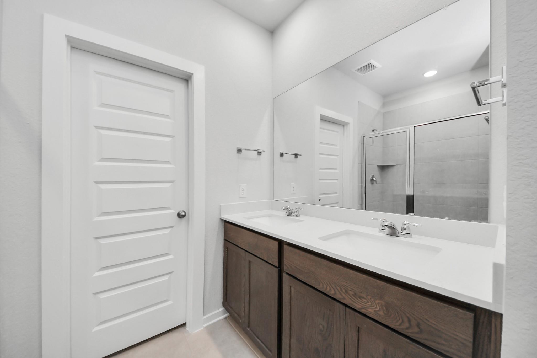 Modern dual-vanity bathroom with dark wood cabinets and glass shower in Davidson Homes The Brazos F floor plan.