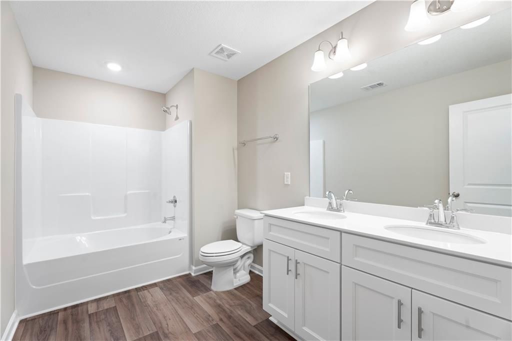 Modern bathroom featuring white shower, deep tub, double vanity, and laminate wood floors in Davidson Homes The Washington, Phenix City, Alabama