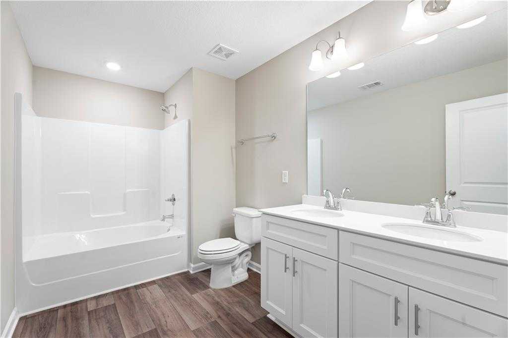 Modern bathroom with white tub-shower combo, double vanity, and wood floors in Davidson Homes The Washington, Phenix City, AL