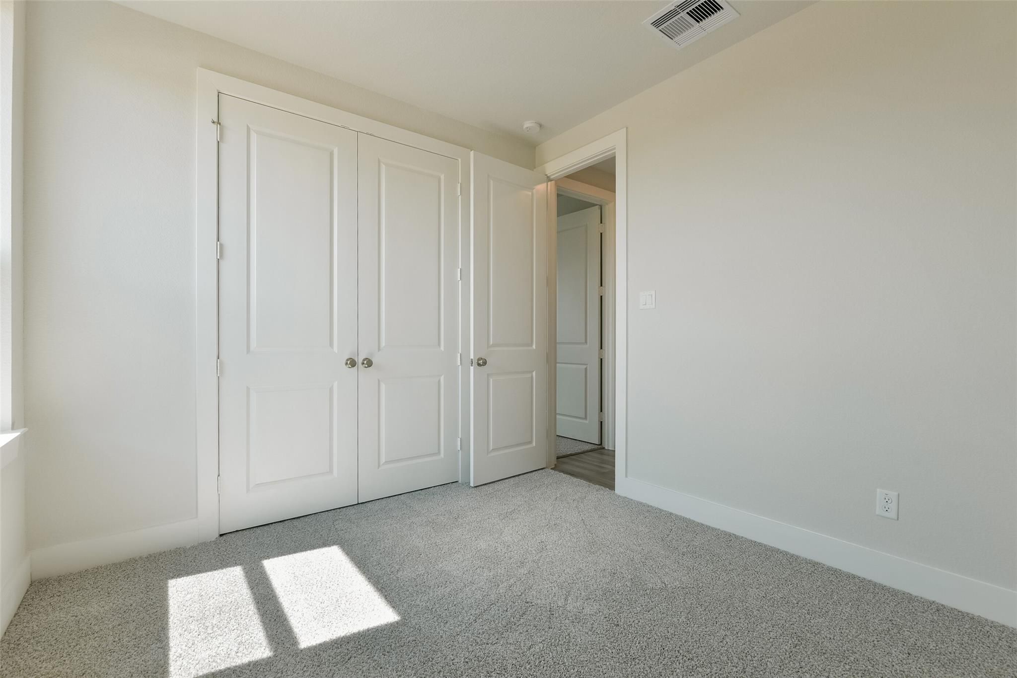 Sunlit secondary bedroom with white bi-fold closet doors and adjacent bath in Davidson Homes The Edward A, Lago Mar, Texas
