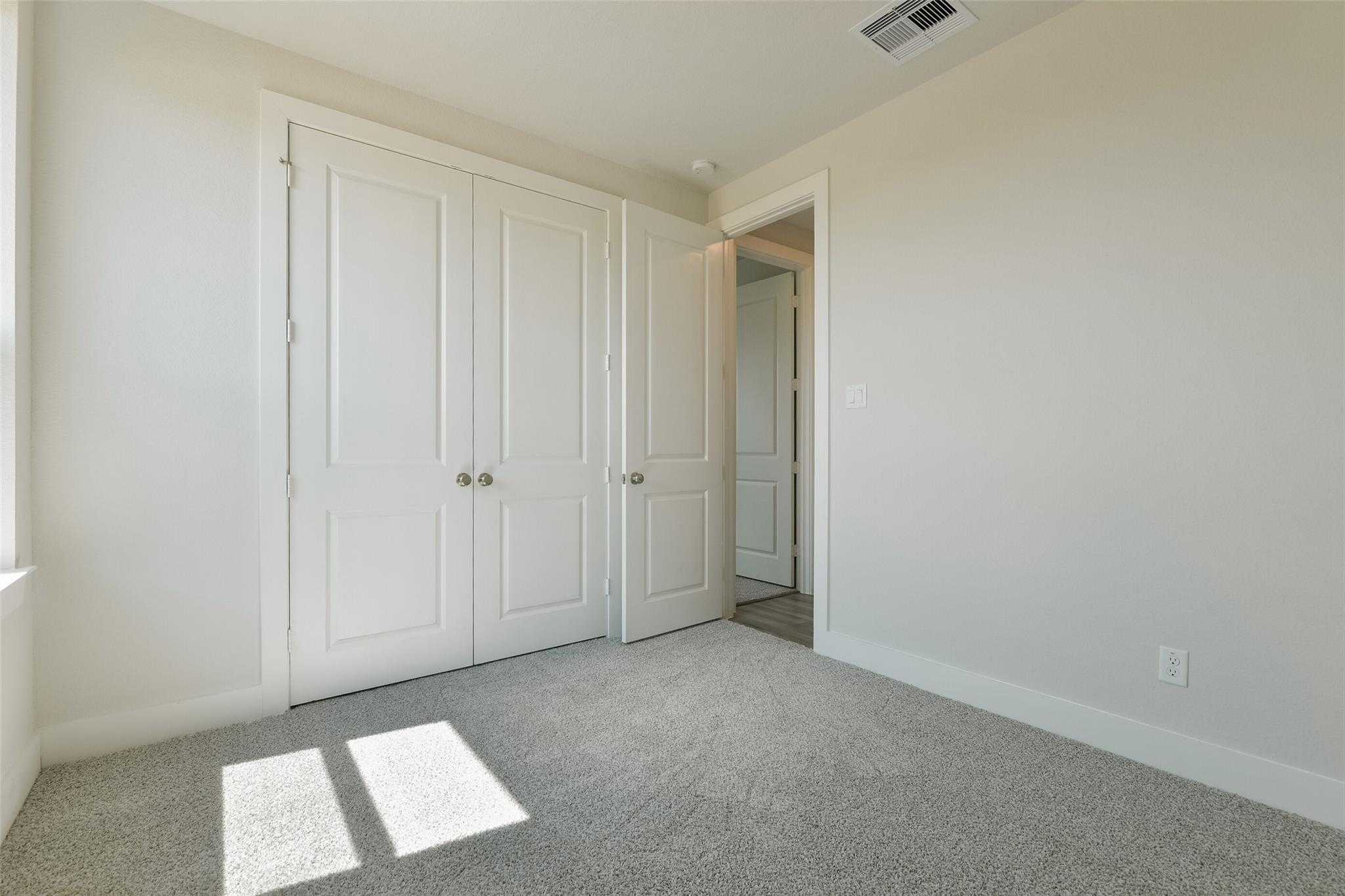 Sunlit secondary bedroom with white bi-fold closet doors and adjacent bath in Davidson Homes The Edward A, Lago Mar, Texas