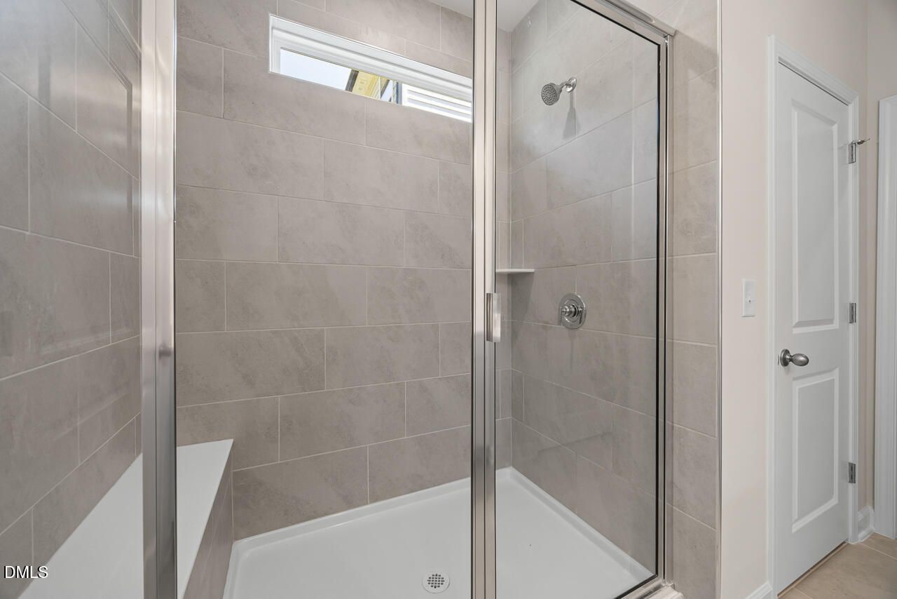 Tiled walk-in shower with glass door, built-in bench, and transom window in Davidson Homes bathroom at Woodland Crossing, Zebulon NC
