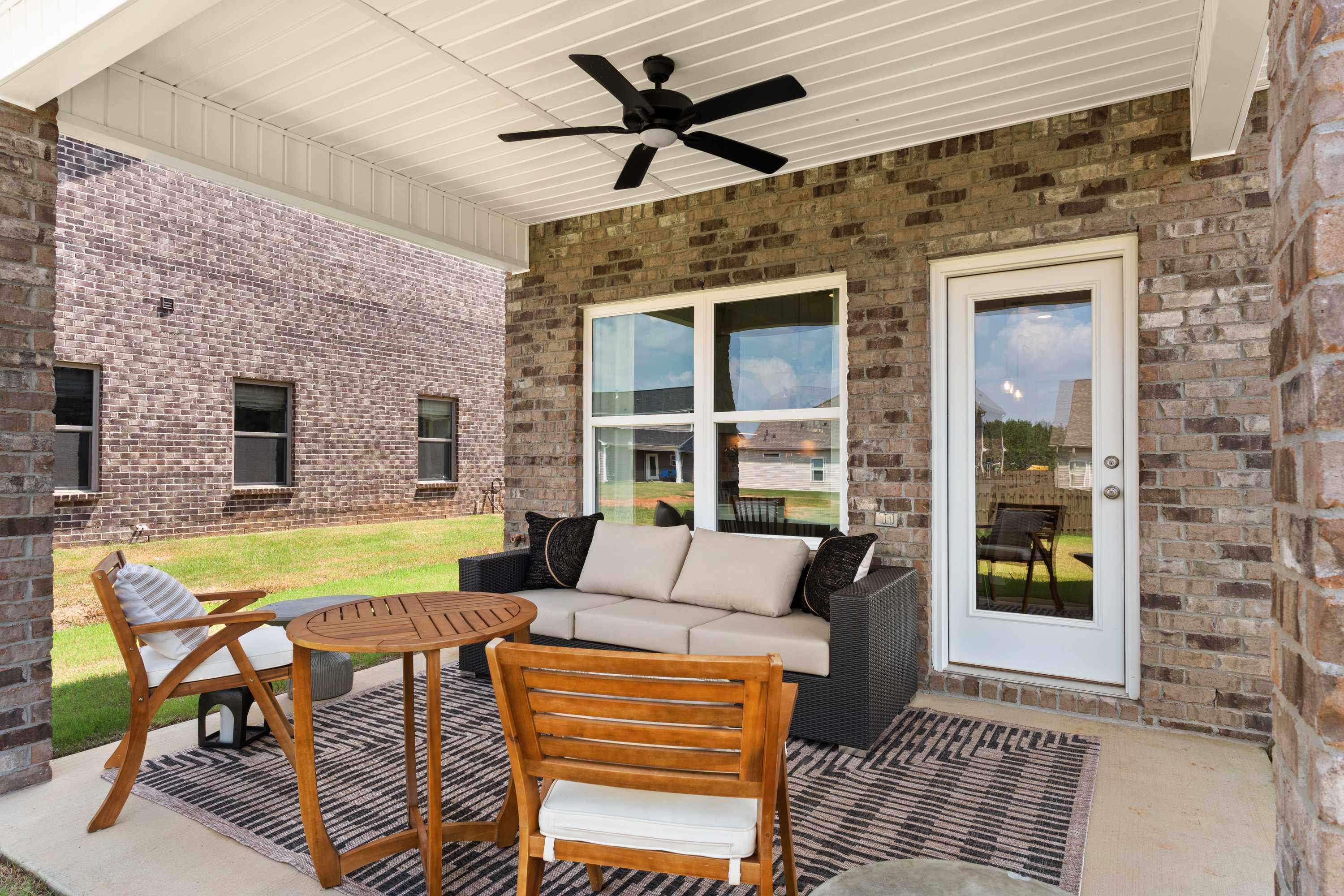 Spacious covered porch of The Shelby A with brick walls, ceiling fan, large windows, glass door, and wicker outdoor seating in Meridianville Alabama