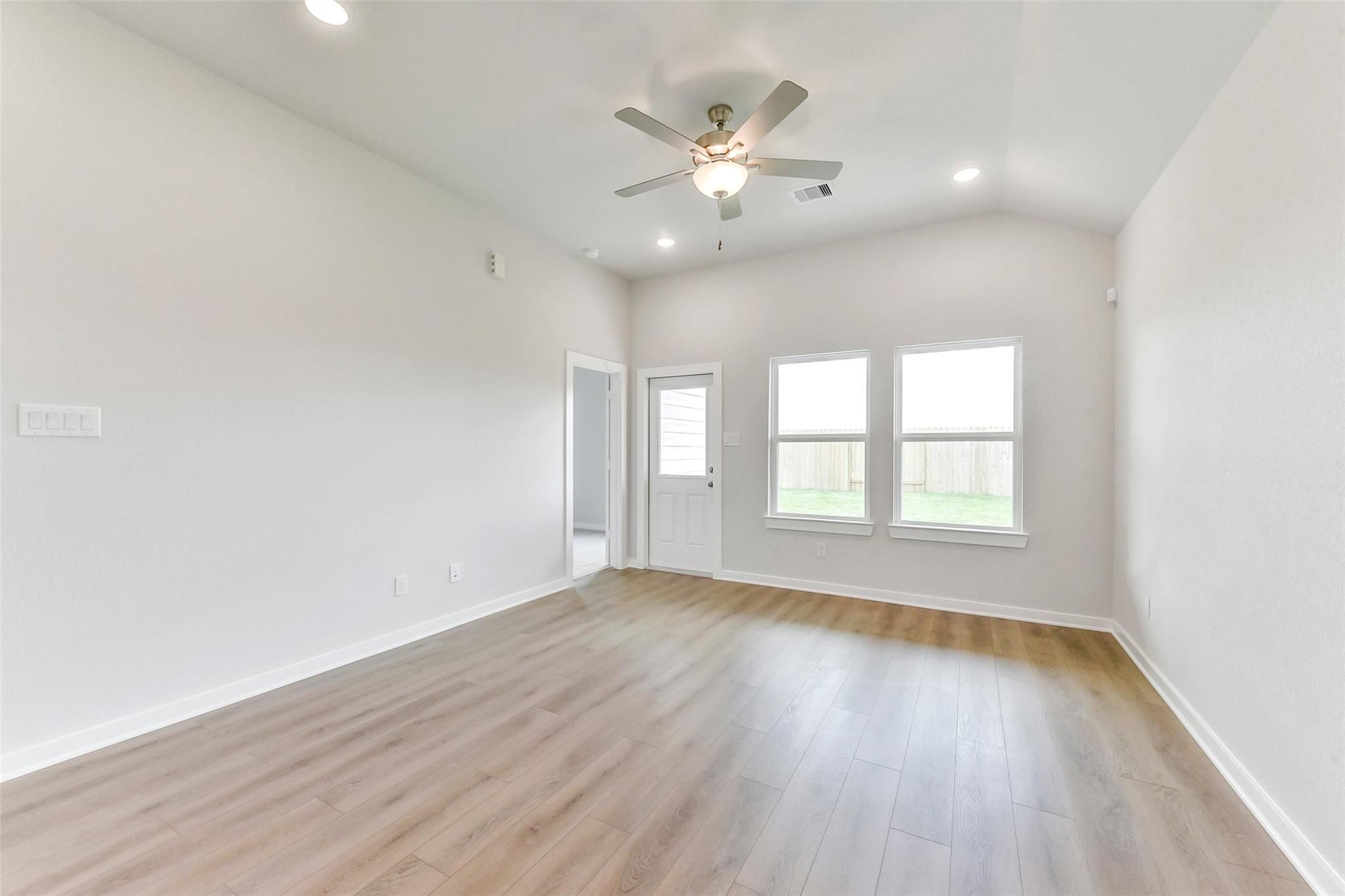 Bright living room with ceiling fan, large windows overlooking fenced backyard in Davidson Homes The Costa B, Dayton, Texas