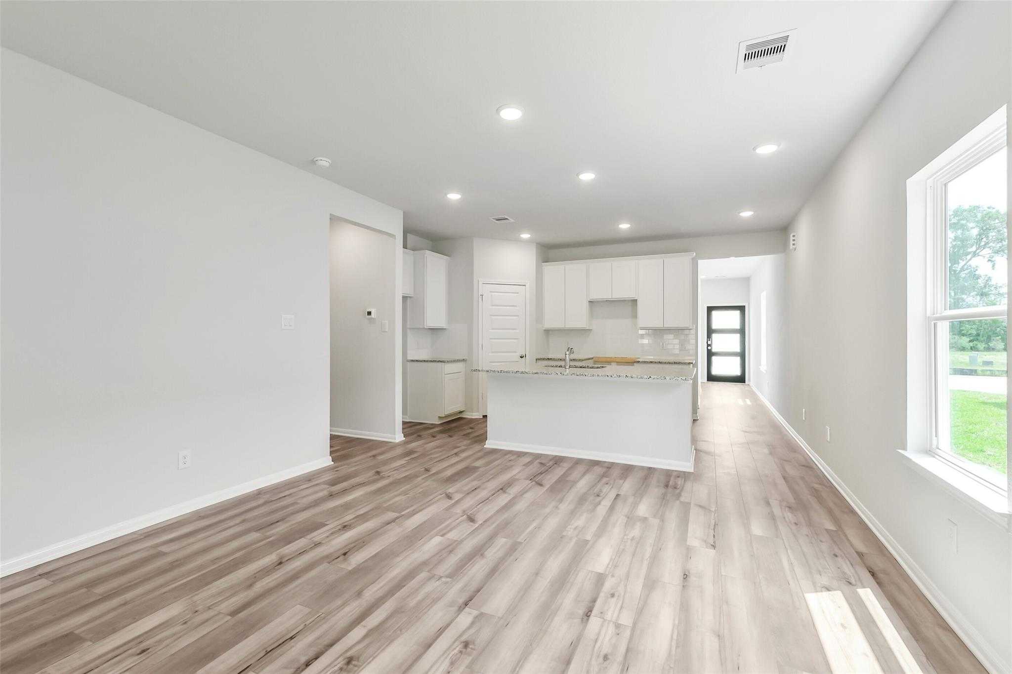 Spacious open-concept kitchen and living area with white cabinets, center island, and hardwood floors in Davidson Homes The Sabine E, Conroe, Texas